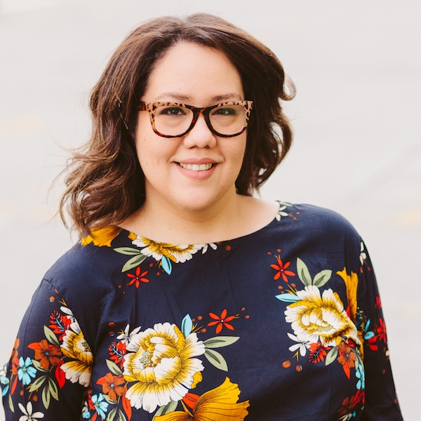 Arivel Figueroa headshot wearing blue blouse with yellow and red flowers as well as tortoise shell glasses